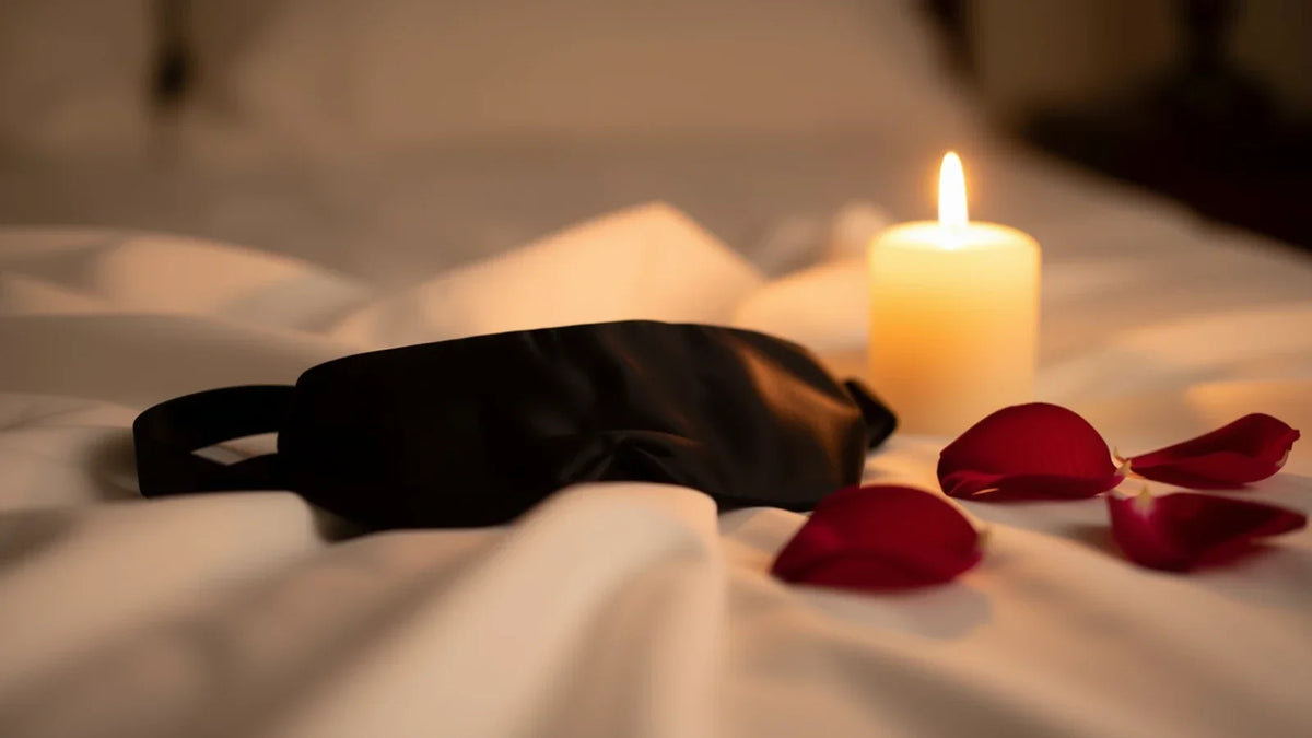 Bandeau de satin, bougie et pétales de rose sur un lit, ambiance préliminaires